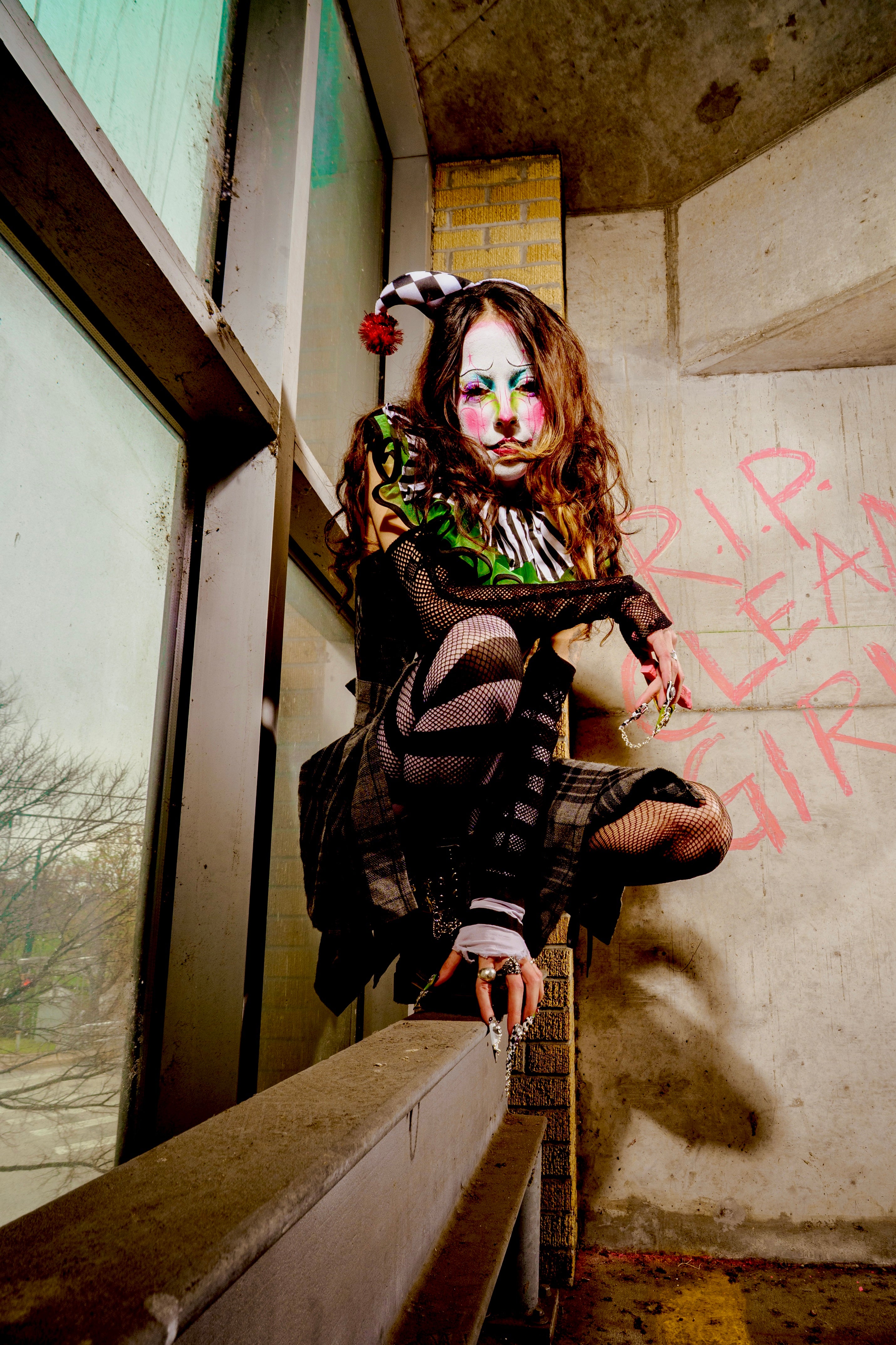 Person with artistic makeup sitting on a ledge in an urban setting with graffiti.